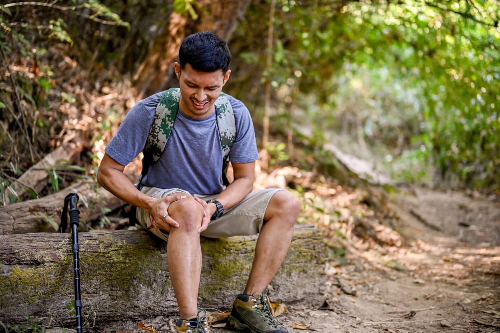 Man sitting outdoors holding his knee in pain after a hiking injury